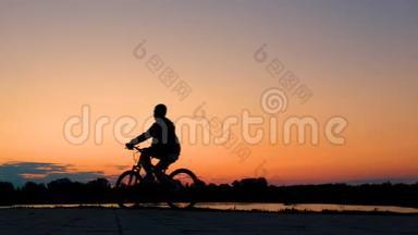 一个少年清晨在黎明或傍晚在日落时骑着自行<strong>车</strong>骑过河流或湖泊。 一辆自行<strong>车</strong>的<strong>剪影</strong>